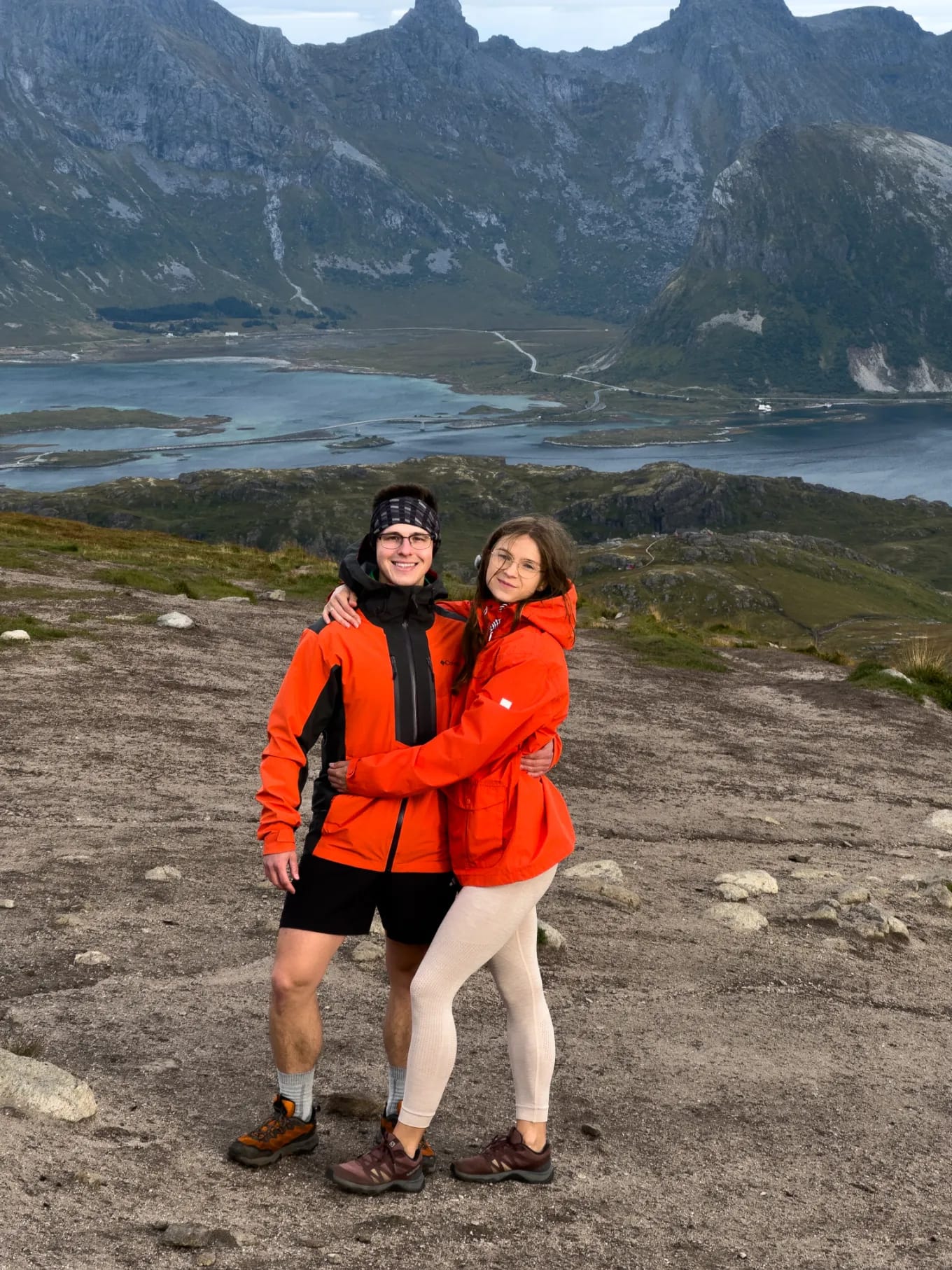 Para turystów na szczycie Ryten z widokiem na plaże i góry Lofotów